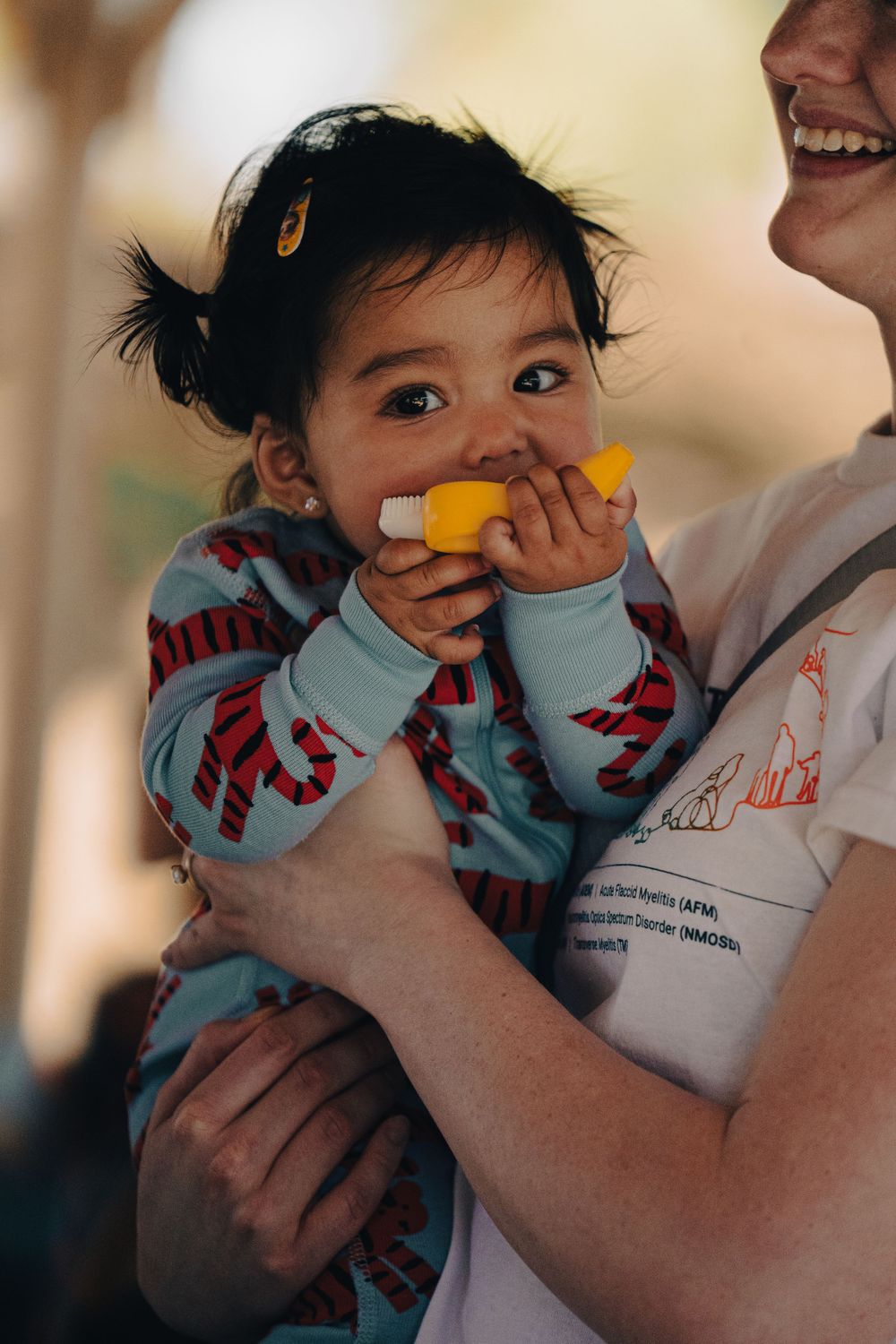 A toddler in patterned clothing eating while being held.