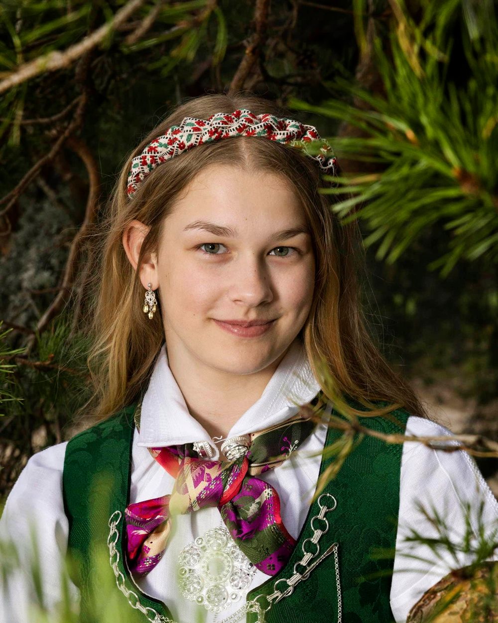 Jente i bunad og hårbånd som ser i kamera og smiler lurt i Mandal