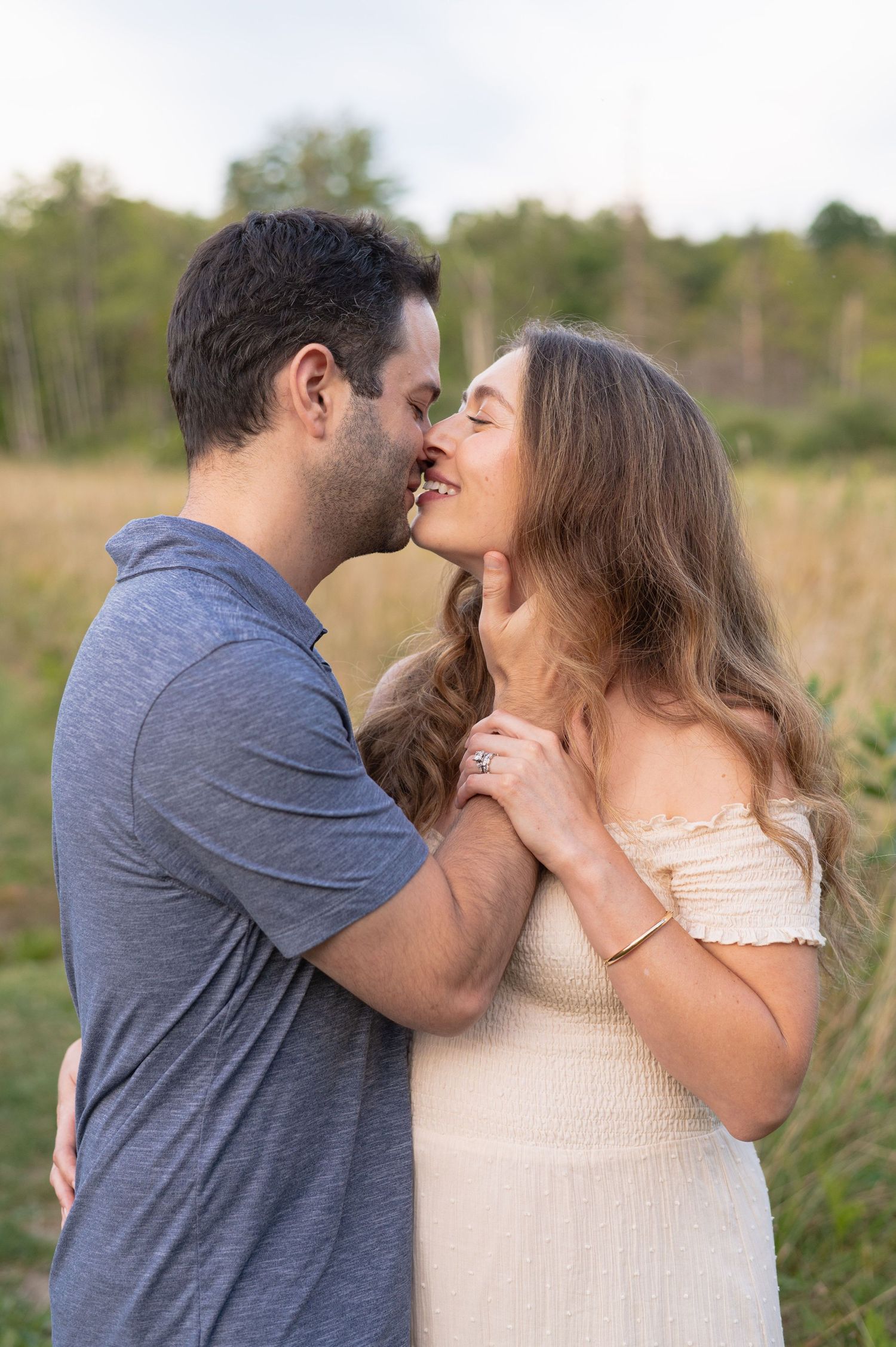 A romantic moment between a couple embracing in a sunlit field wearing a grey shirt and cream dress.