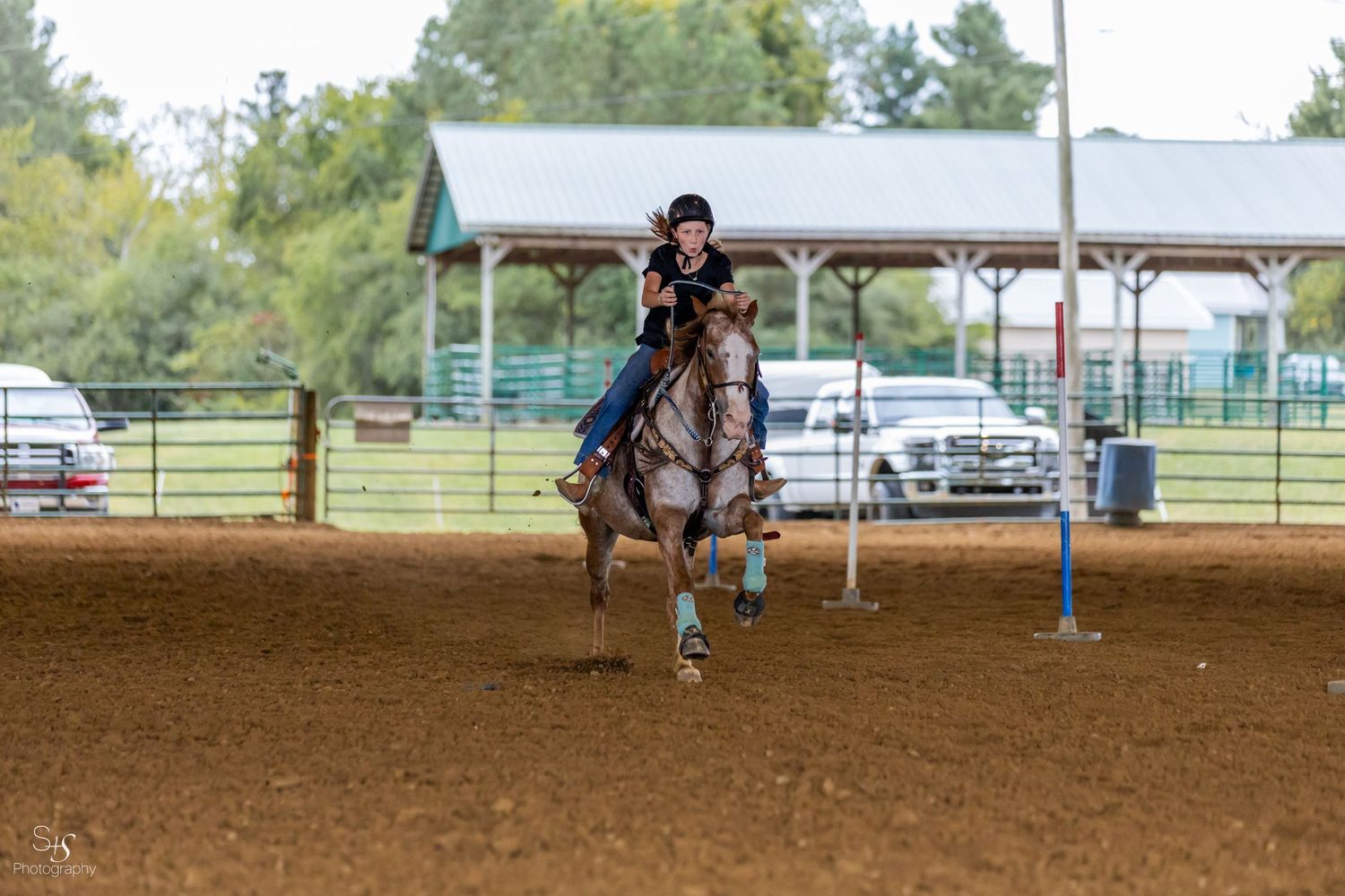 Horse and rider racing around barrel in dusty arena during competition.