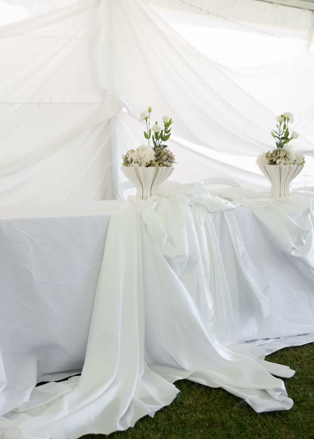 Elegant white draped fabric and floral arrangements create a sophisticated wedding ceremony setup outdoors.