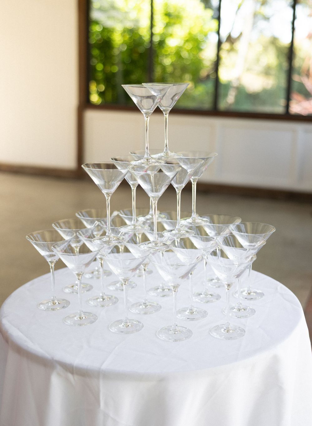 Elegant martini glasses stacked in a pyramid formation on a round white tablecloth for a special event or celebration.