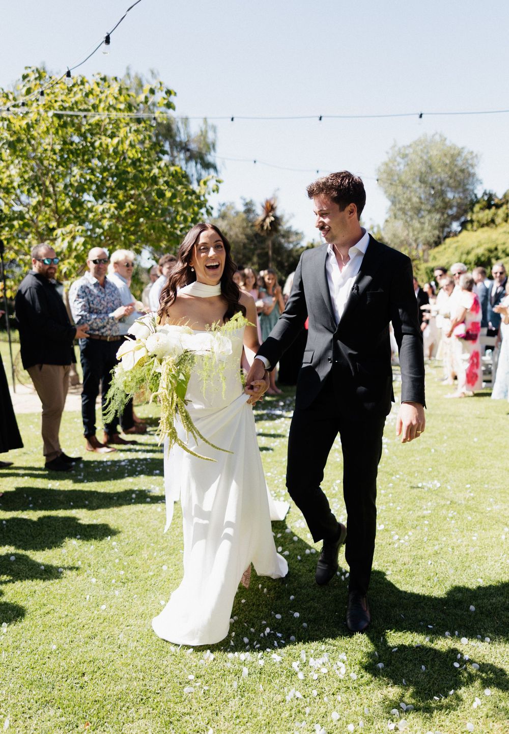 A couple walking together on a grassy lawn during their outdoor garden wedding celebration.