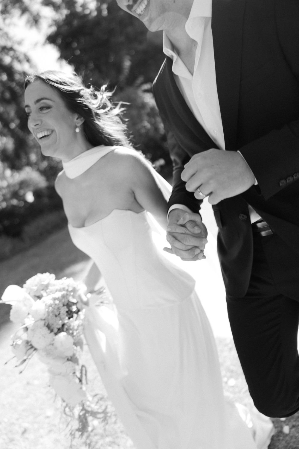 A black and white wedding photo capturing a candid moment of laughter in a garden setting.