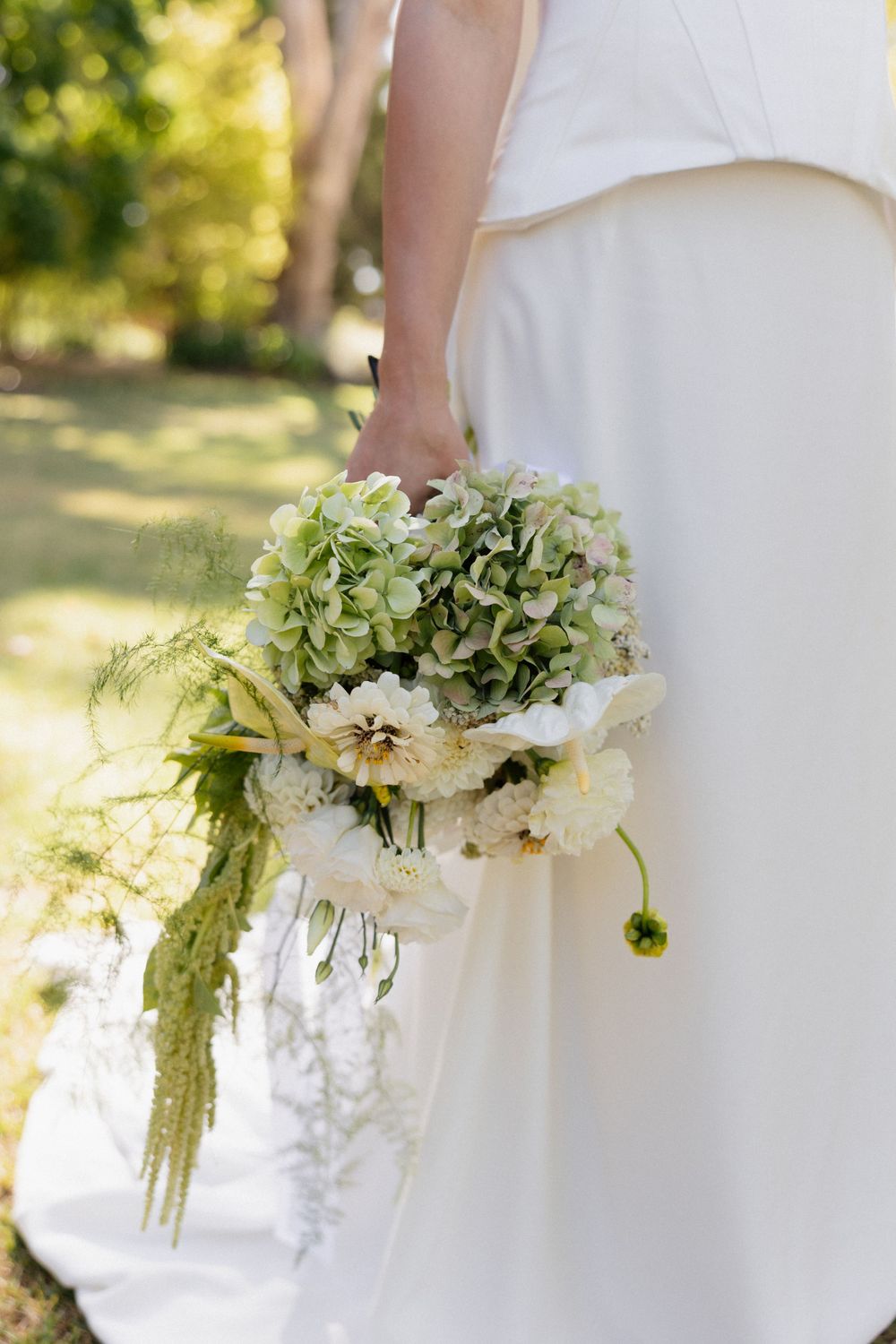 A bridal bouquet features white and green hydrangeas with cascading greenery against a flowing white dress.