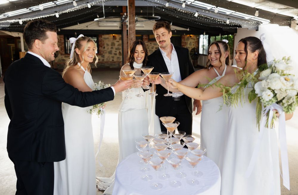 Wedding party toasts with champagne glasses around a tiered tower of coupe glasses at an elegant reception.