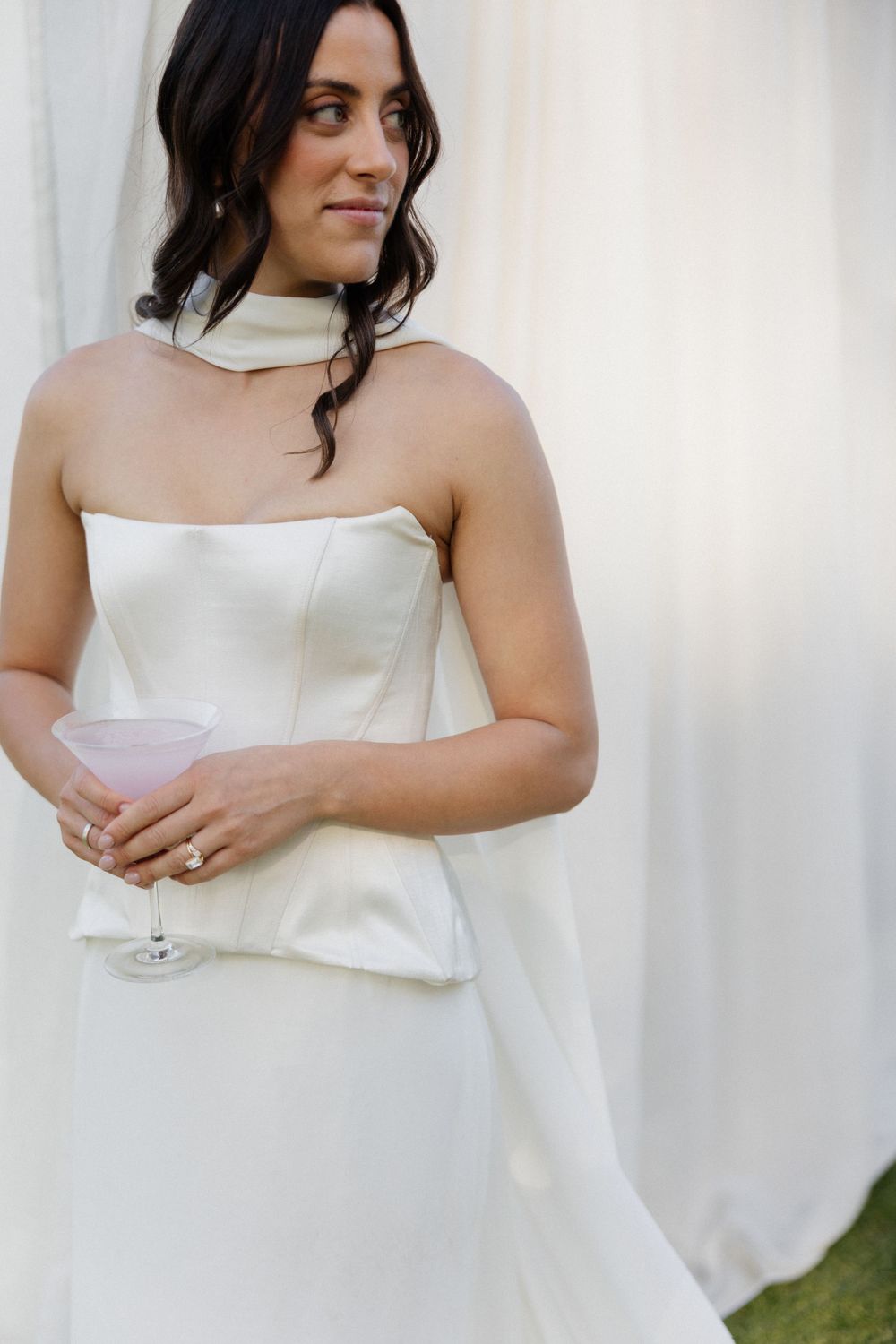 Elegant bride in a strapless white gown holds champagne glass at outdoor wedding celebration.