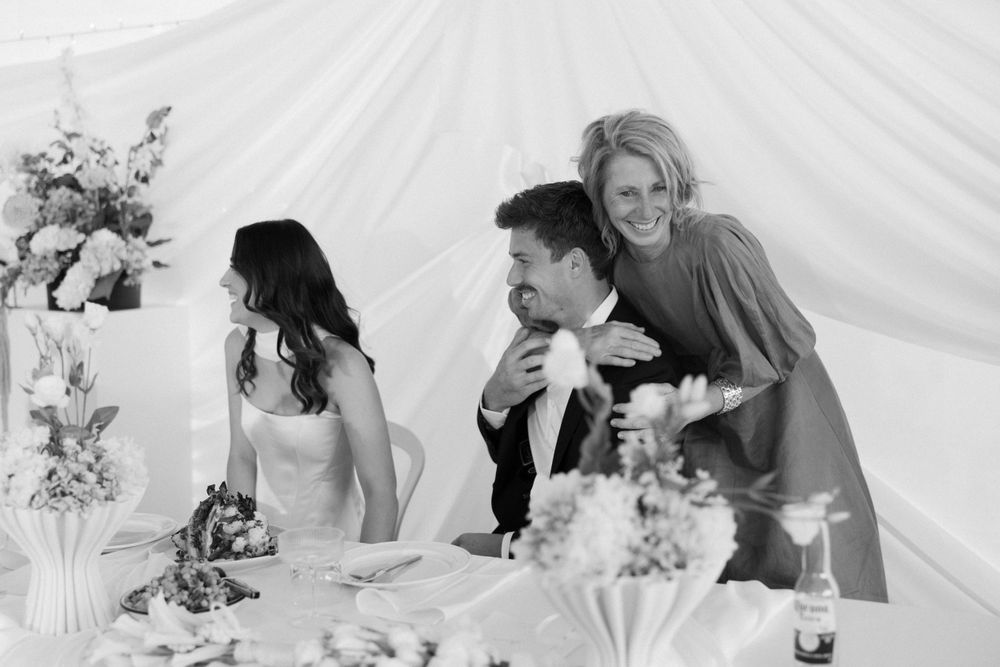 A wedding reception moment captured in black and white under a white tent with floral decorations.