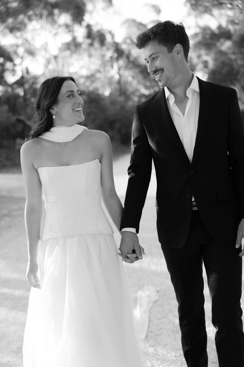 A happy couple shares a loving moment in black and white, the bride in a white dress and groom in dark suit holding hands.
