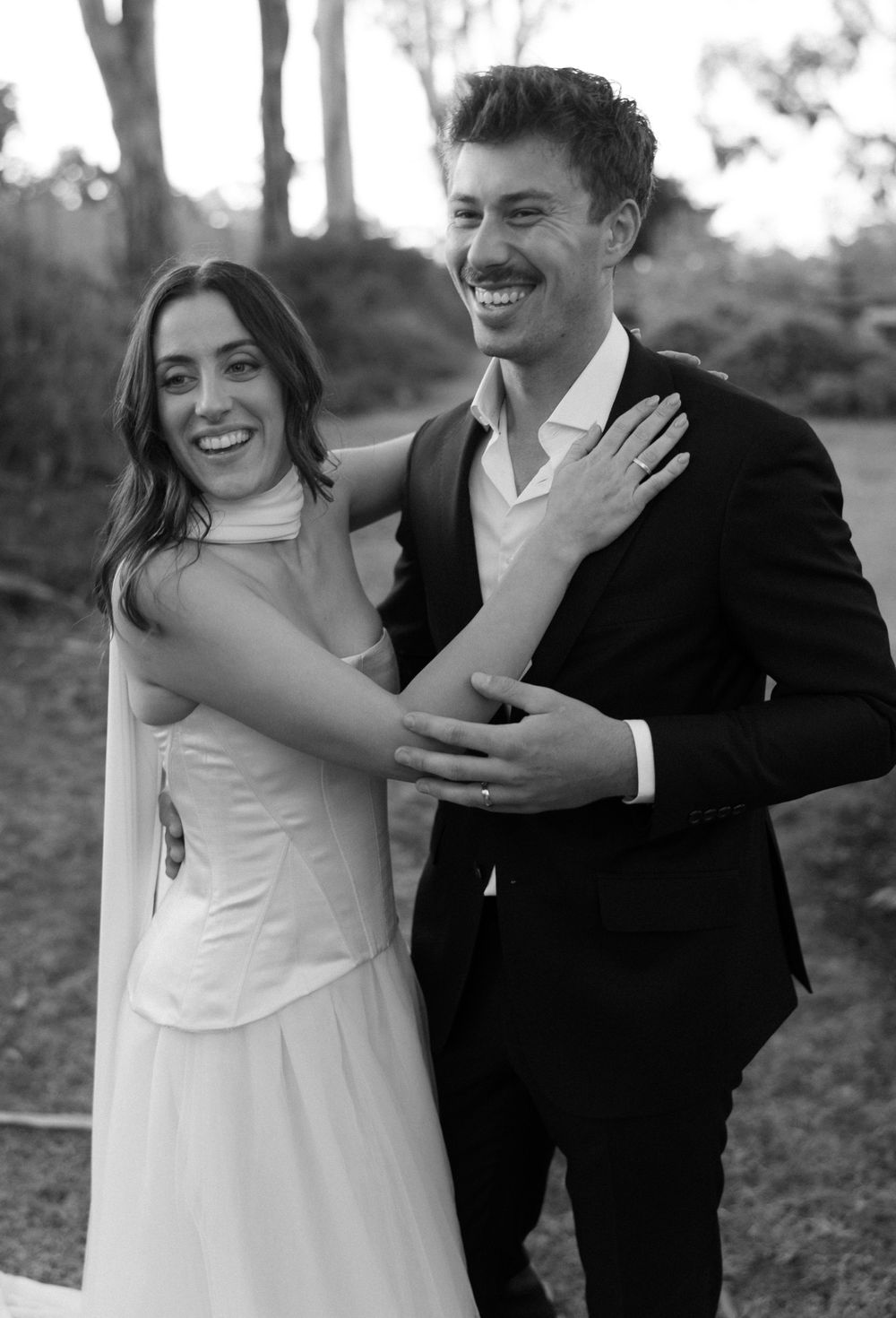 Black and white wedding portrait shows couple embracing and smiling outdoors.