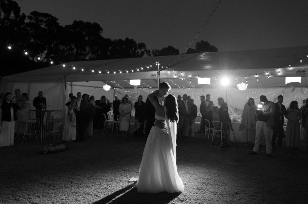 A couple shares their first dance at an outdoor evening reception under twinkling string lights.
