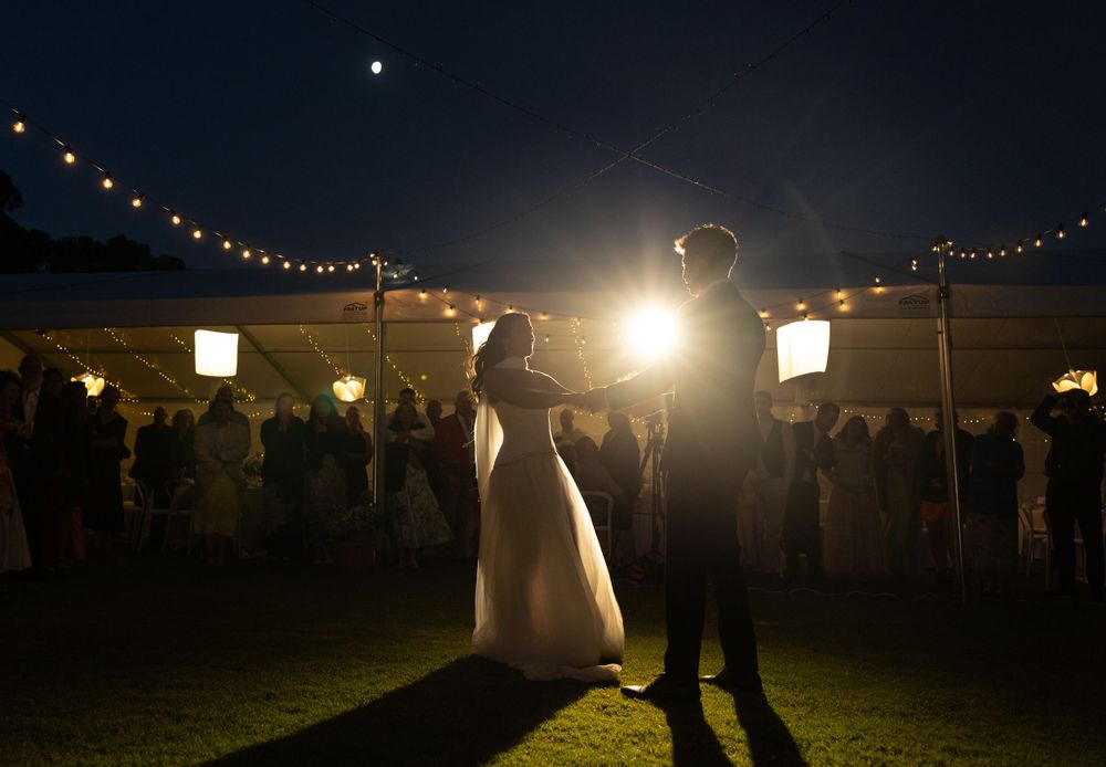 A silhouetted couple dances beneath romantic string lights at an outdoor evening wedding reception.