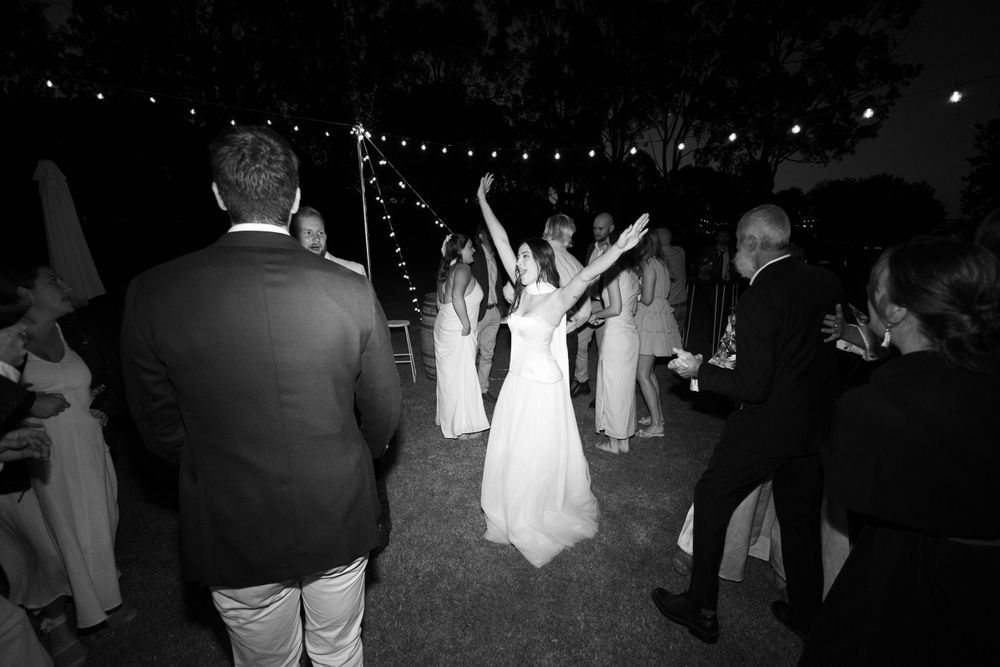 Wedding guests dance and celebrate under market lights at an outdoor nighttime reception.