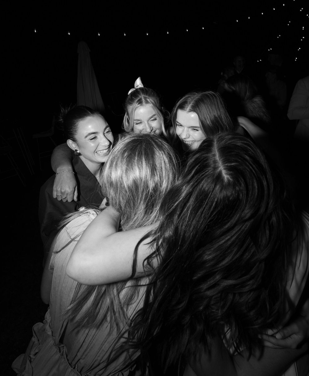 Friends sharing a joyful group hug during a nighttime wedding celebration.