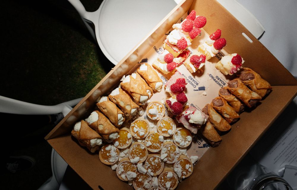 Appetizer platter with assorted pastries and desserts topped with fresh raspberries on a wooden board.