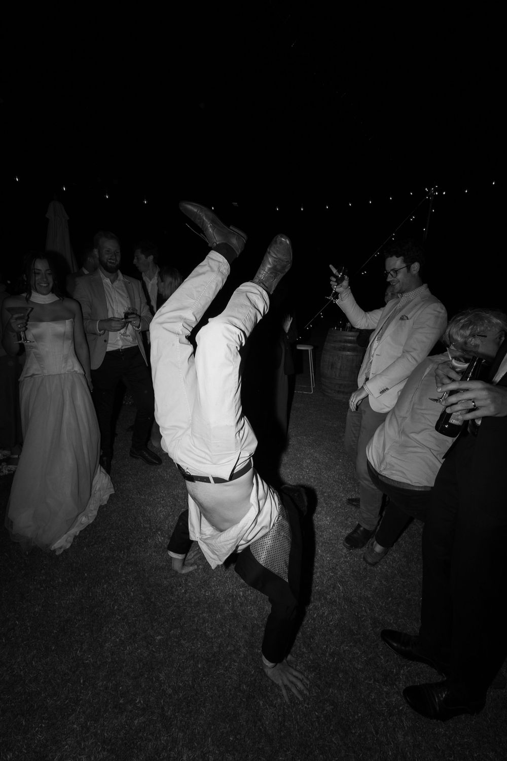 A person in white formal attire performs an impressive breakdancing handstand move during a dance party at night.