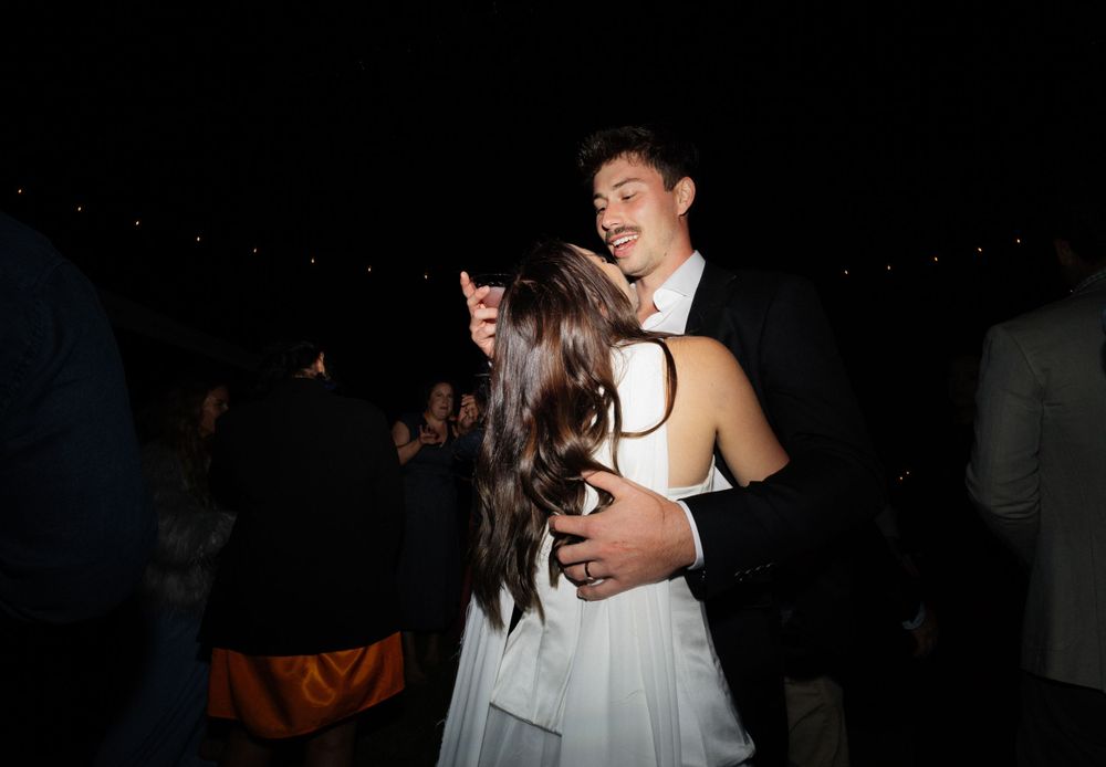A couple in formal attire dances together at a wedding reception in a dimly lit venue.