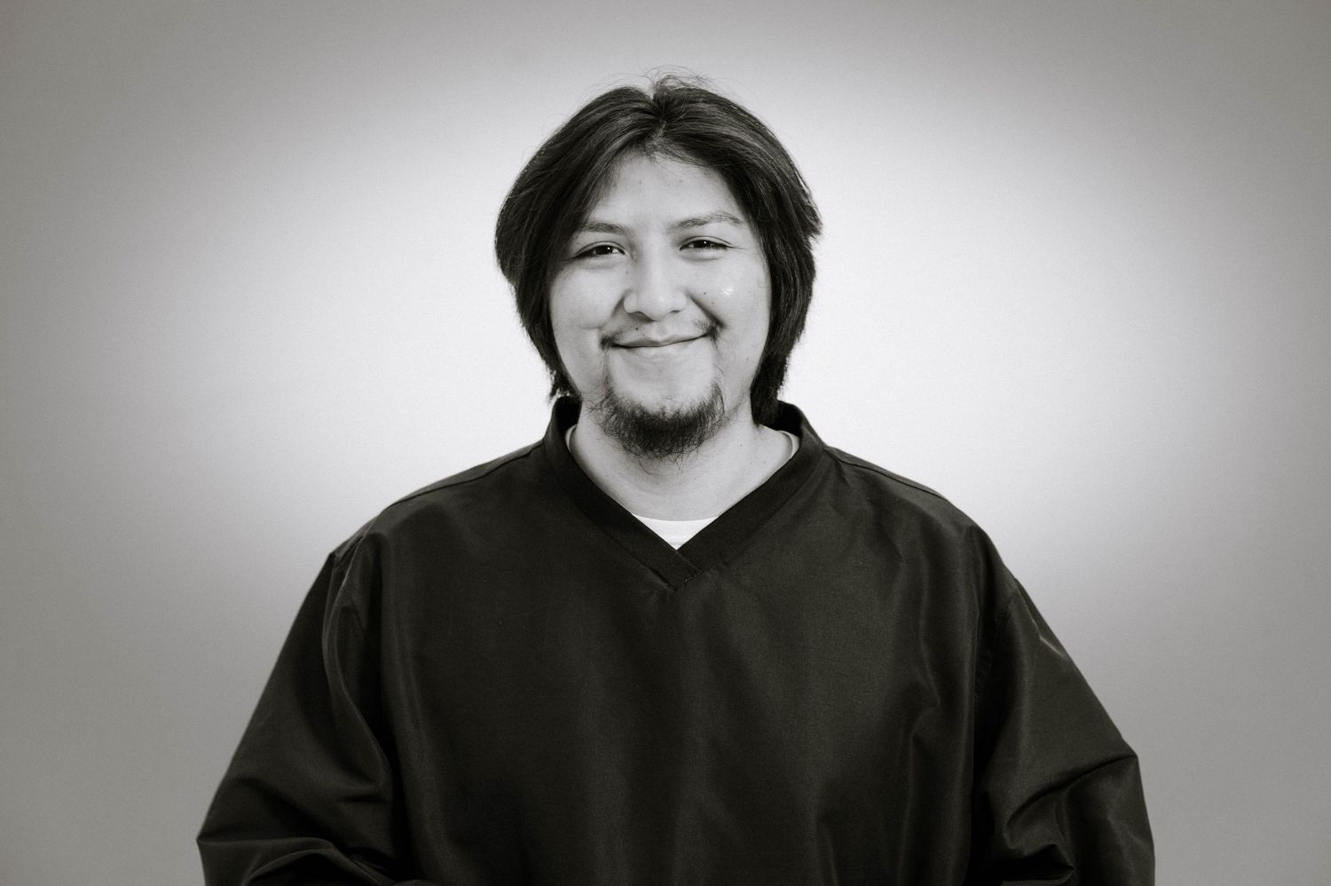 A grayscale portrait photo shows someone wearing a dark v-neck sweater and sporting facial hair.