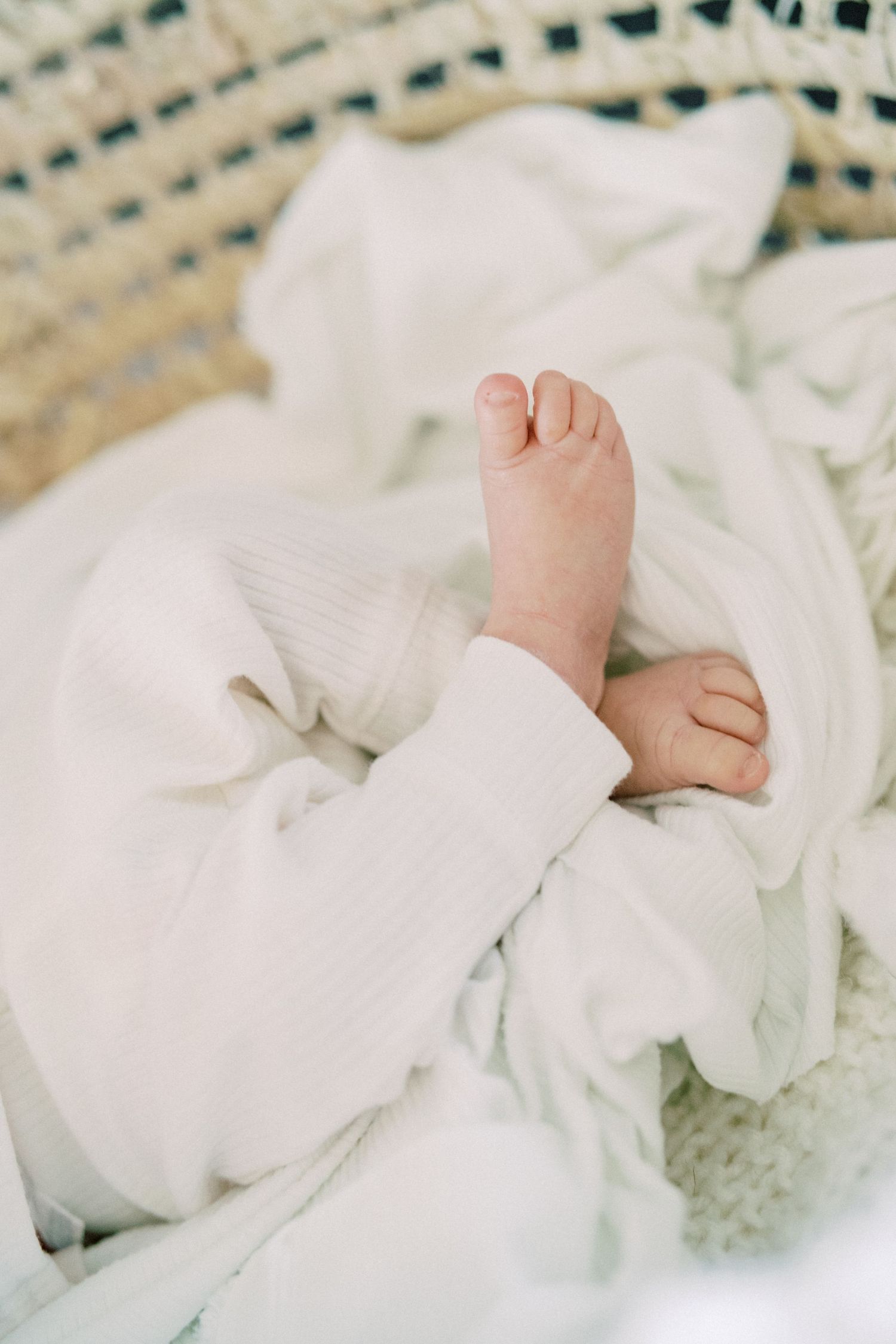 Small baby foot peeking out from white blankets in woven basket.