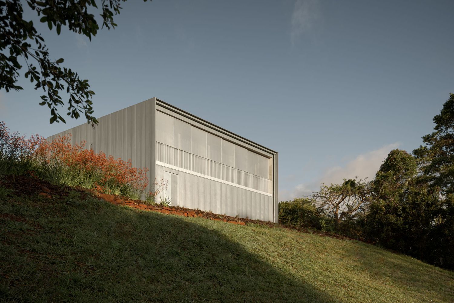 Minimalist architectural structure on grassy hillside with metal cladding.