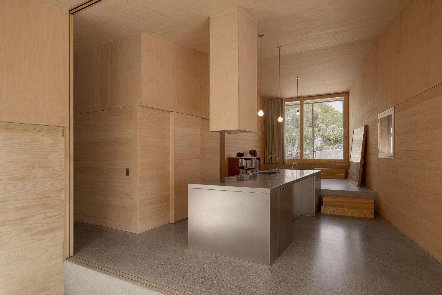Modern kitchen interior with plywood walls and stainless steel island in neutral tones.