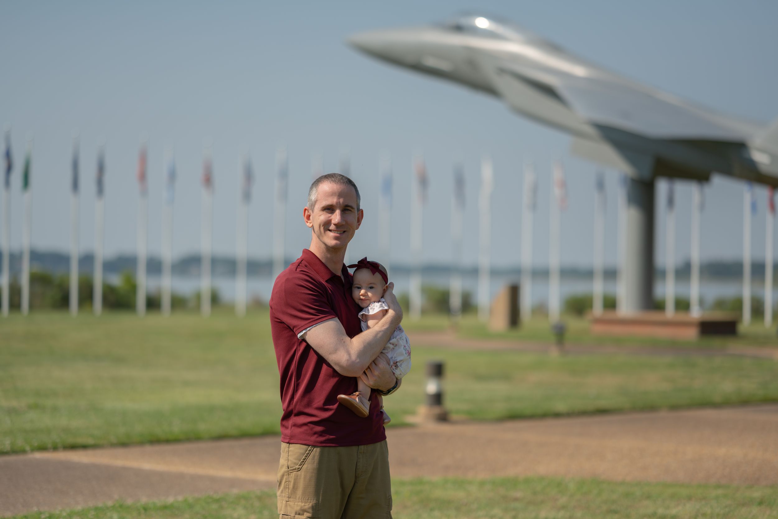 Someone standing outdoors on a sunny day near an aircraft display with rows of international flags visible.