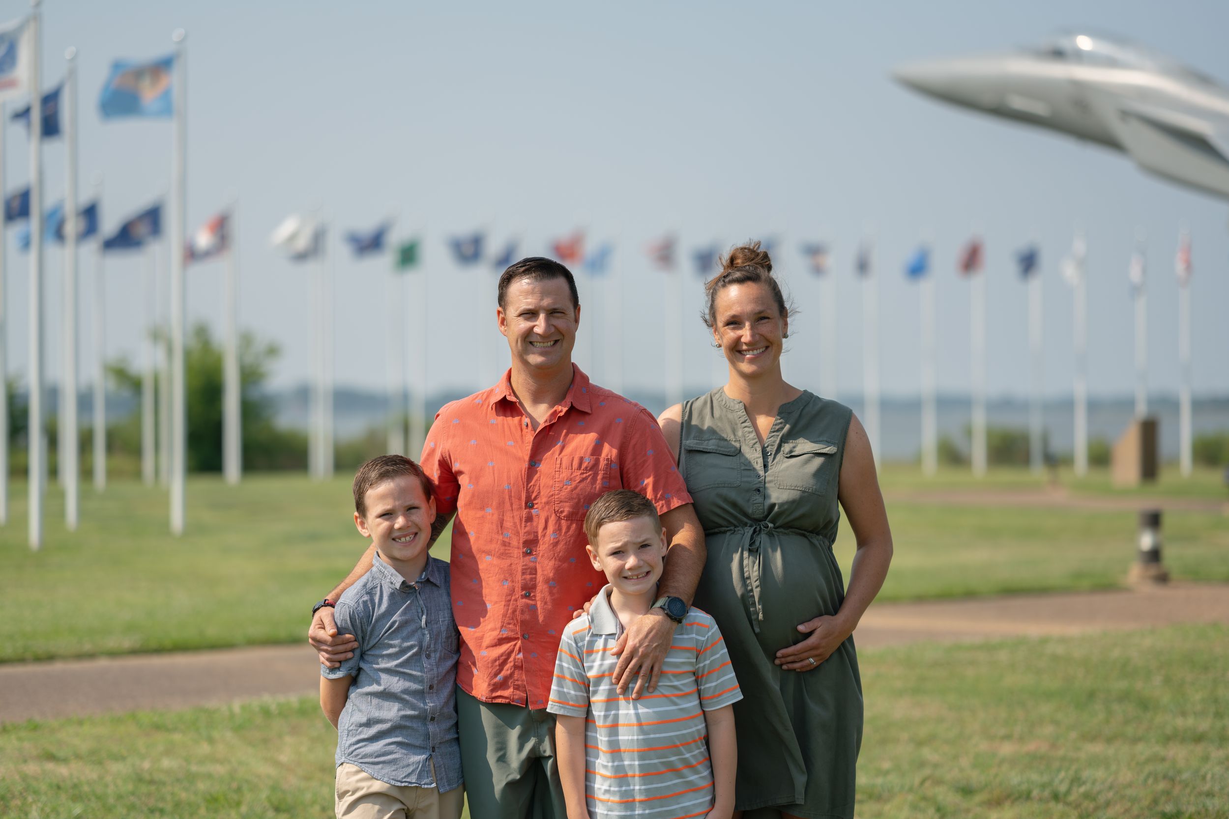 A family group poses together for a photo in front of military aircraft and flag displays on a grassy field.