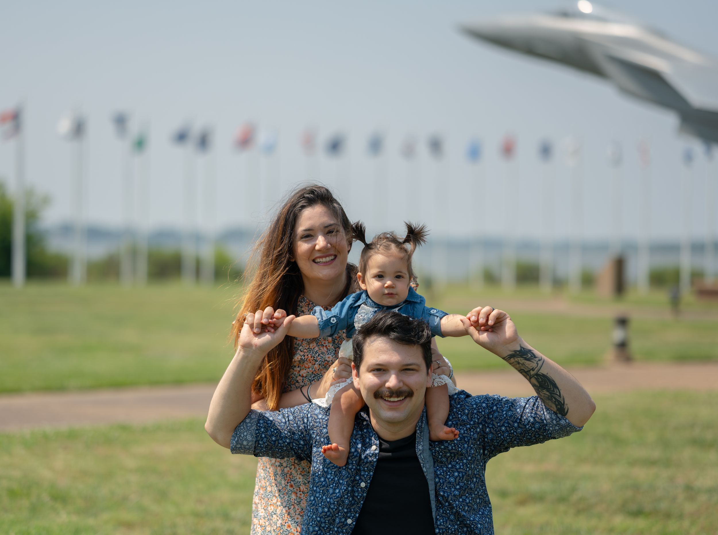 Happy family enjoying outdoor time together at a park with colorful flags flying in the background.