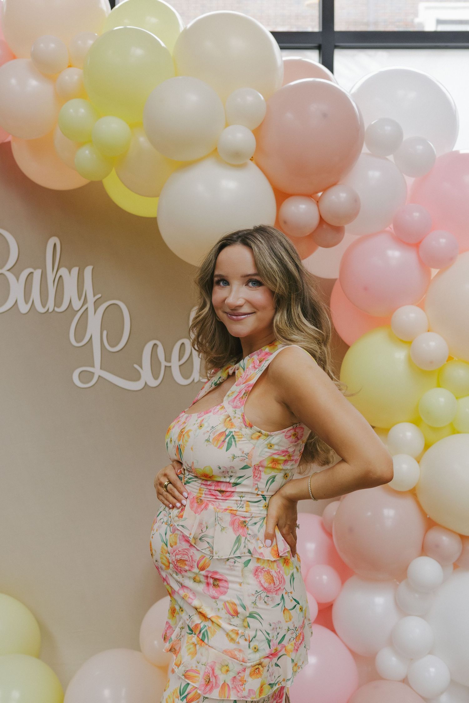 Mom-to-be proudly cradling her baby bump in a floral dress, radiating joy at her Brooklyn baby shower.