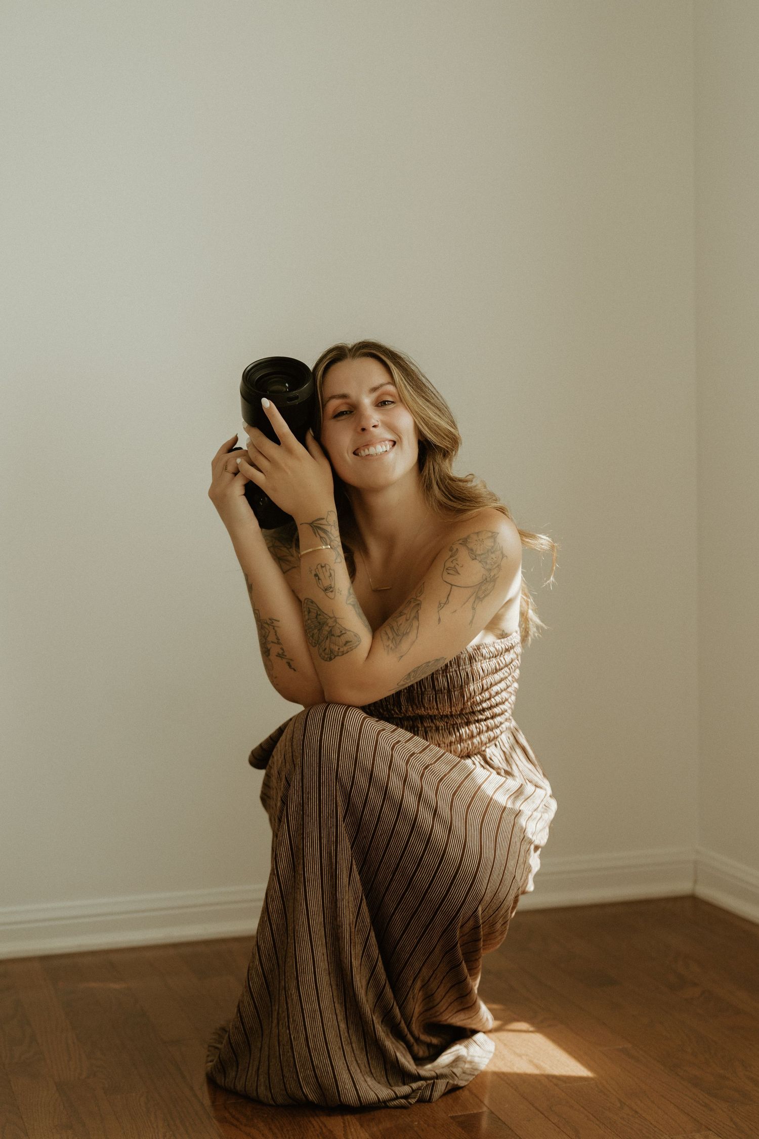 Photographer sitting on tan couch holding professional camera in bright indoor setting.