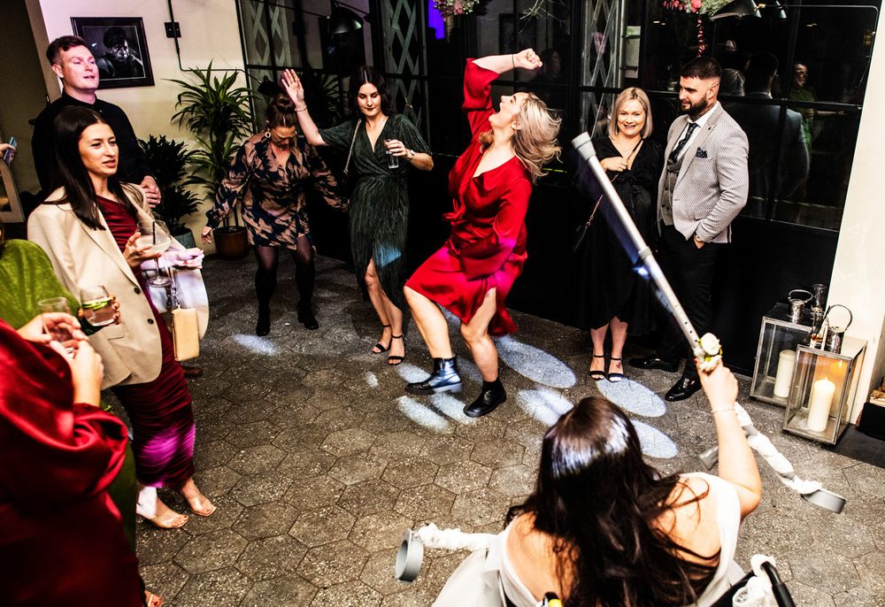 A woman in a red dress dances at a wedding with her arm in the air singing