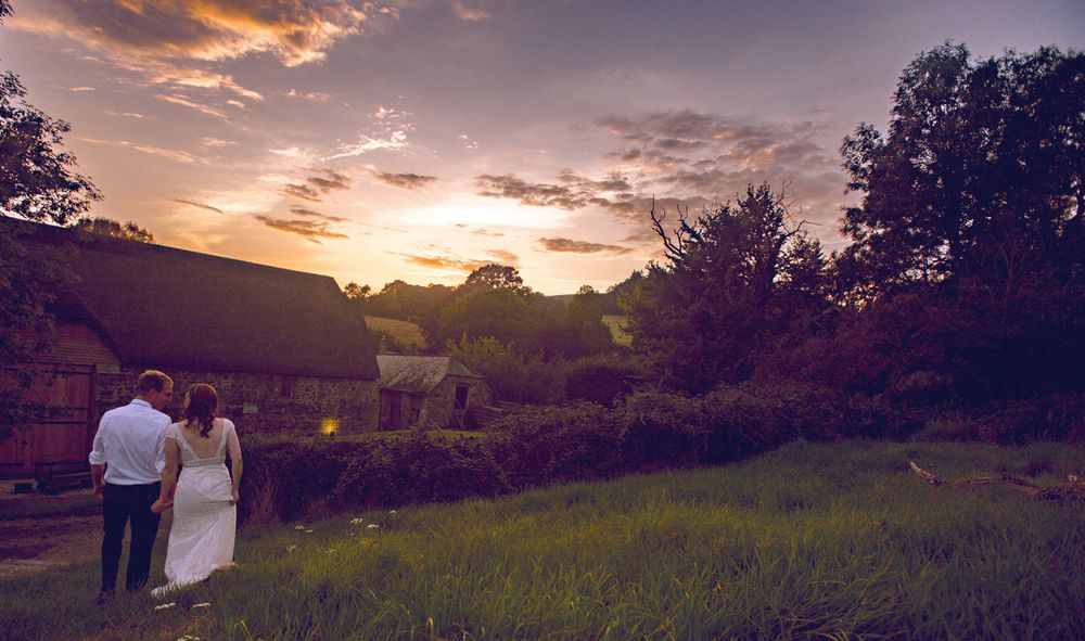 A couple walk hand in hand away from camera at sunset at The Great Barn