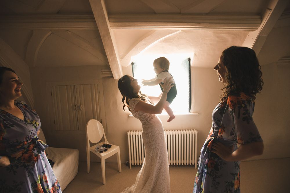 A bride holds up her child in the window back lit light at the Great Barn