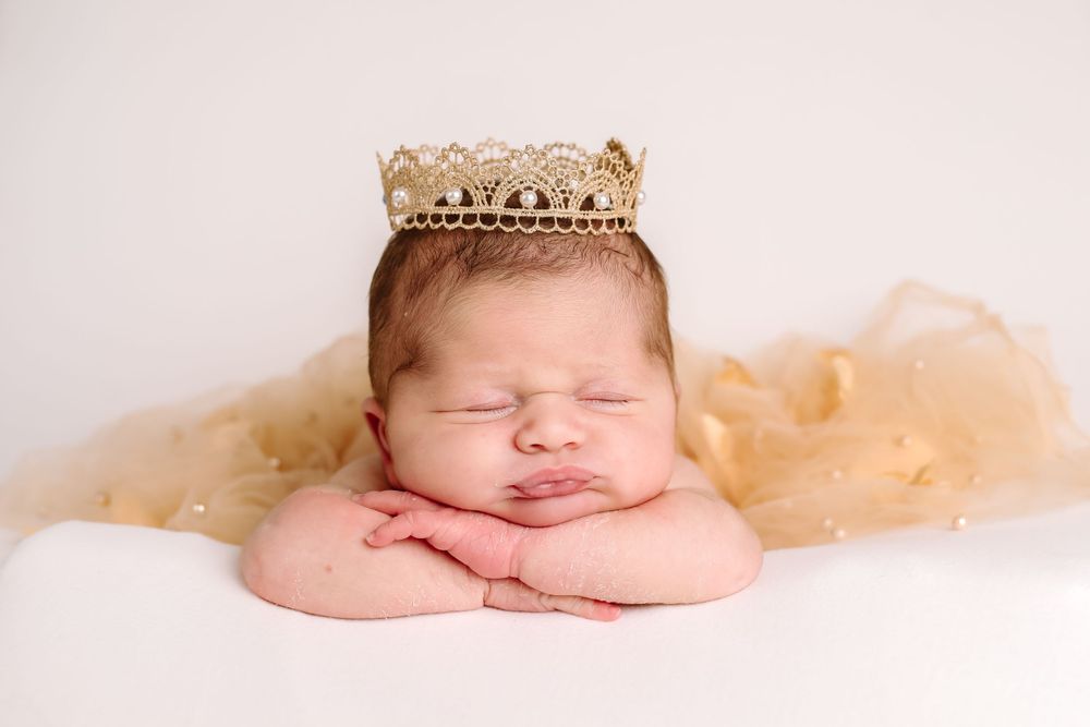 Peaceful sleeping baby wearing gold crown on cream tulle fabric.