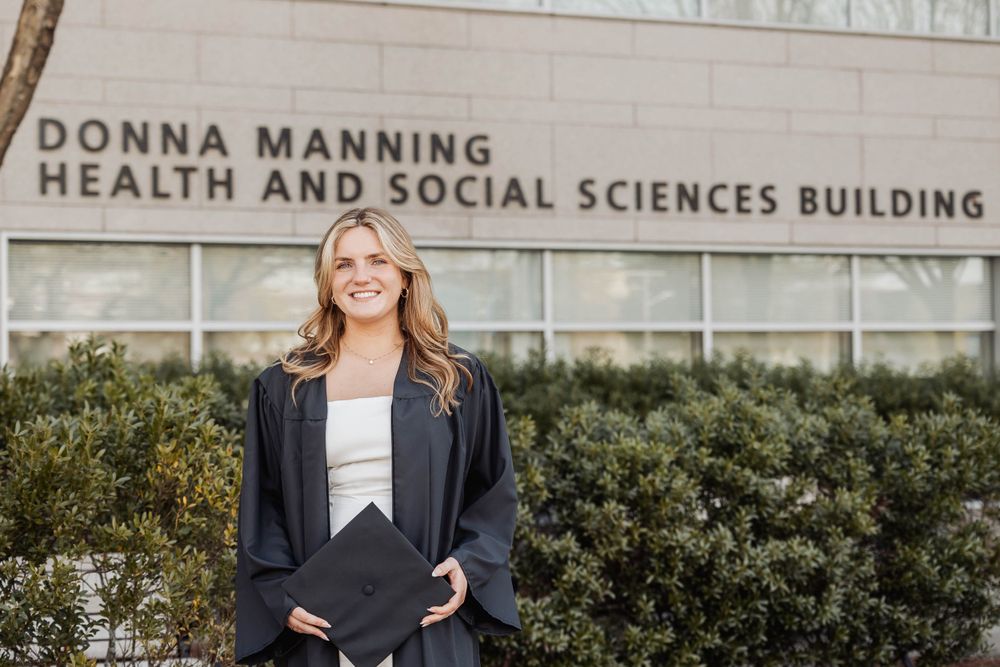 Graduate stands in front of Donna Manning Health and Social Sciences Building.