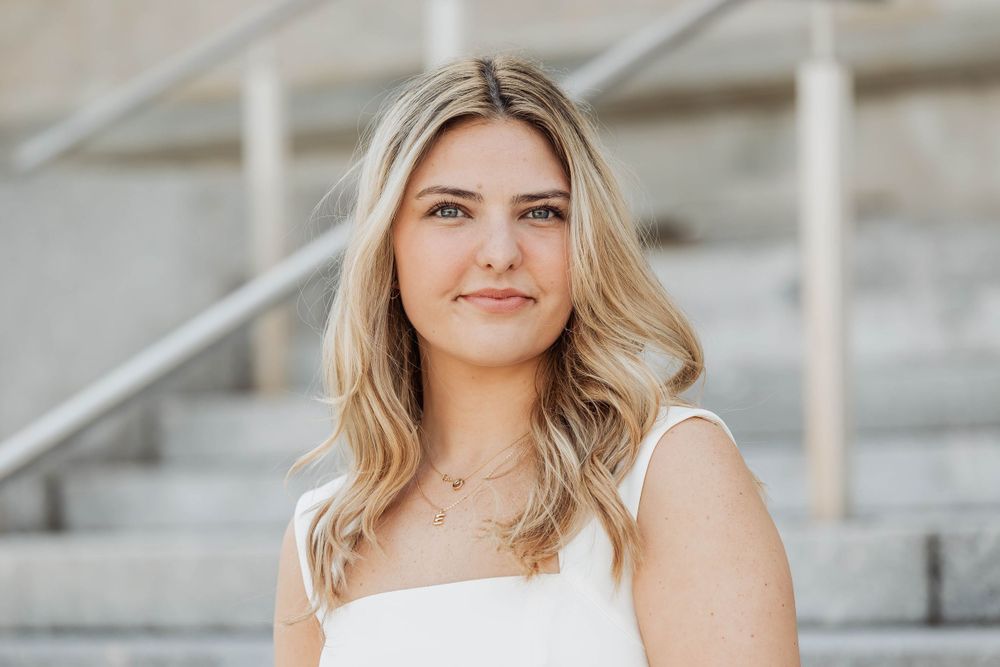 Graduate in white dress poses on concrete steps during graduation photoshoot.