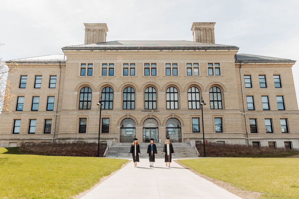 Three small figures walk toward a grand historic stone university building with arched windows.