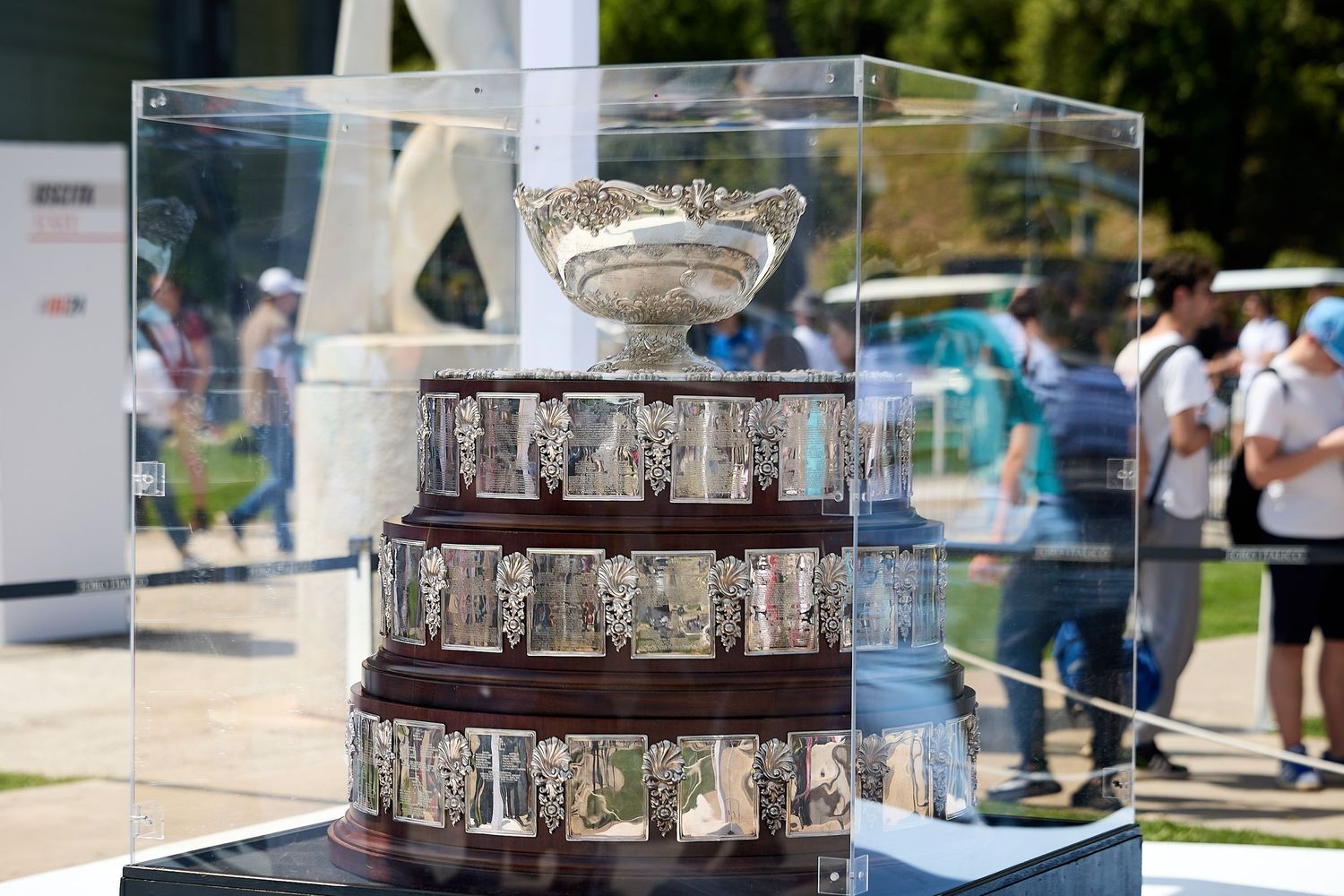 Glass-encased tennis trophies displayed on tiered platform at tournament event.