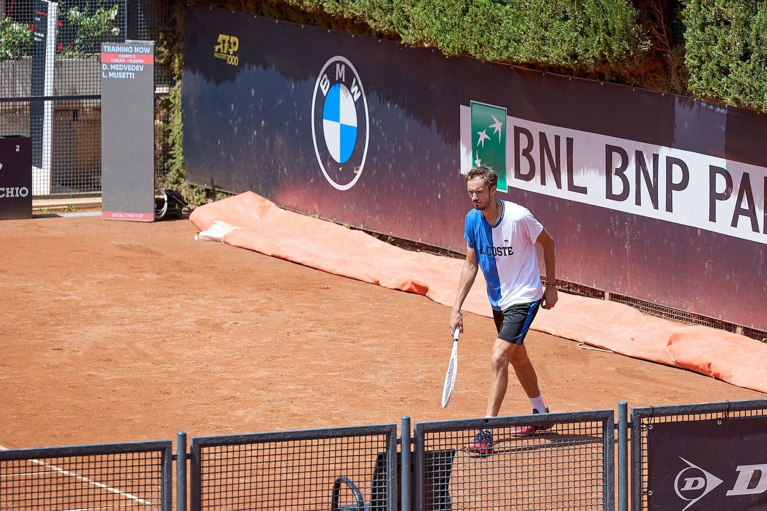 Tennis player practicing on clay court with BMW and BNL BNP Paribas advertising banners visible.