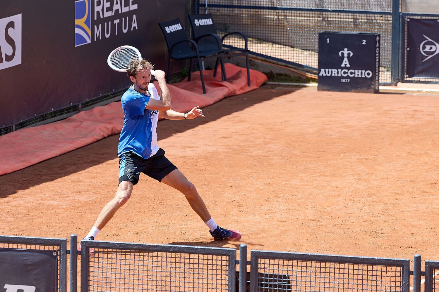 Tennis player hitting overhead shot during match on clay tennis court.