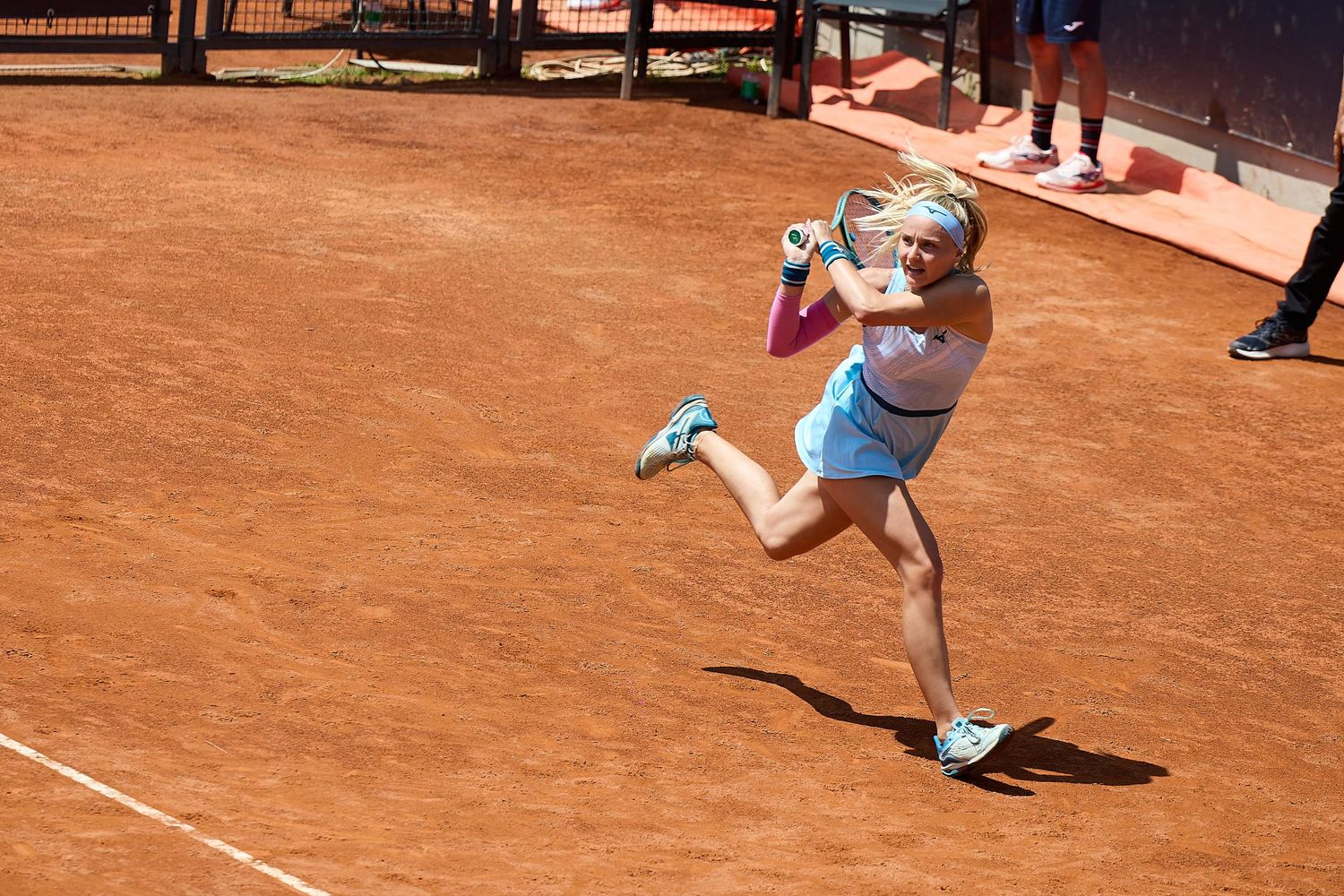 Tennis player in white outfit hits powerful serve on clay court during daytime match.