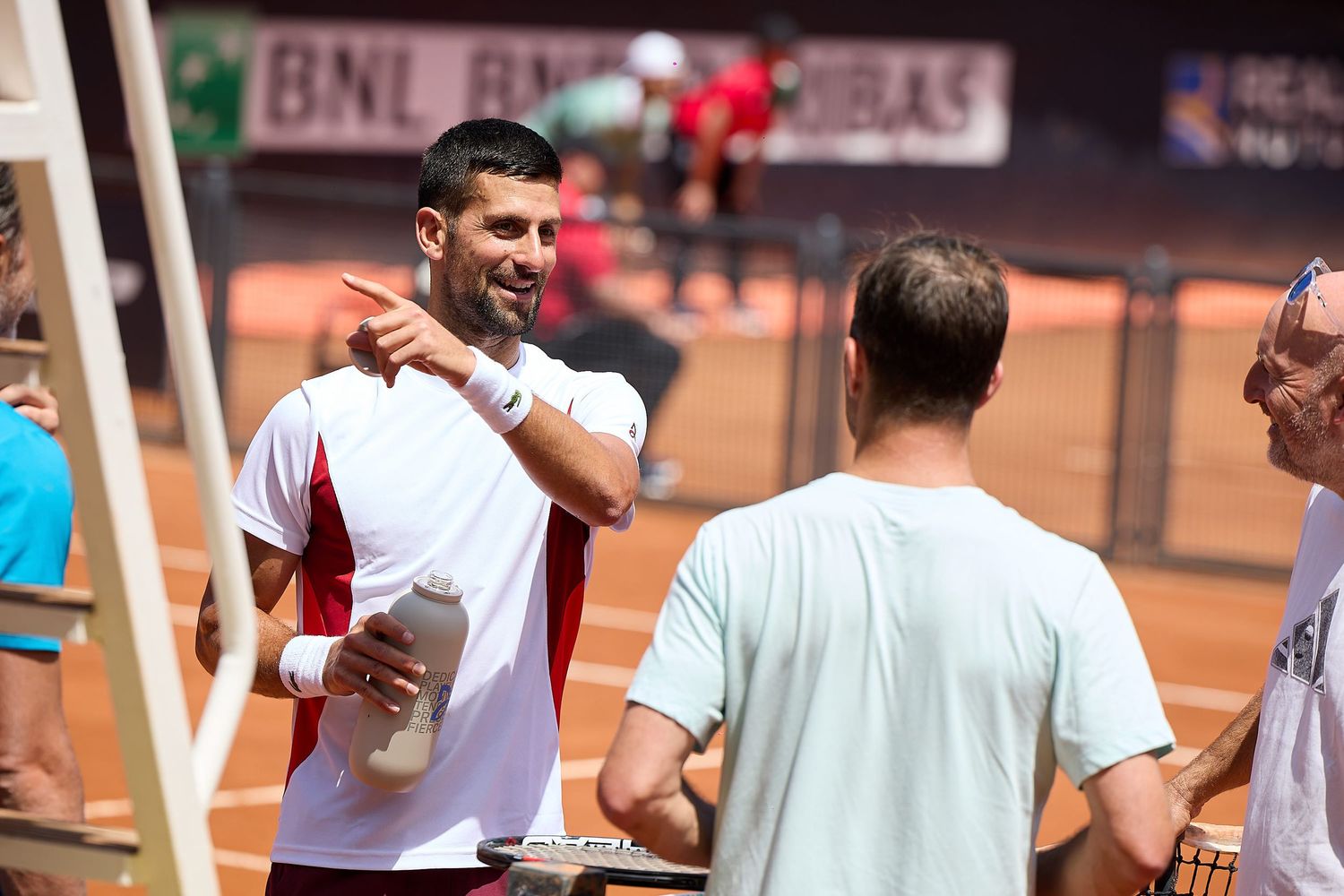 Players having friendly conversation at tennis court sideline during tournament break.