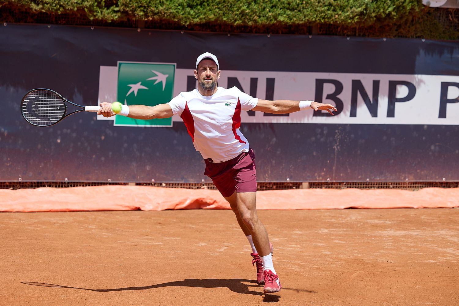 Tennis player executes forehand shot on clay court with BNP Paribas advertising visible.