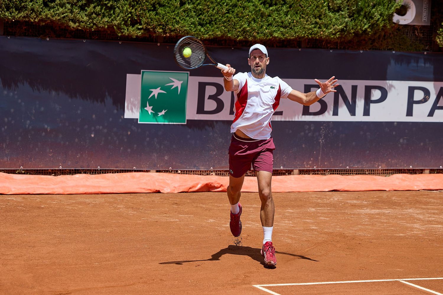 Player jumps while hitting tennis ball on clay court with BNP Paribas signage.