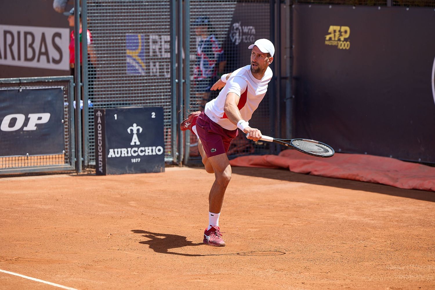 Tennis player serves on clay court with Dunlop and BNP Paribas advertising visible.
