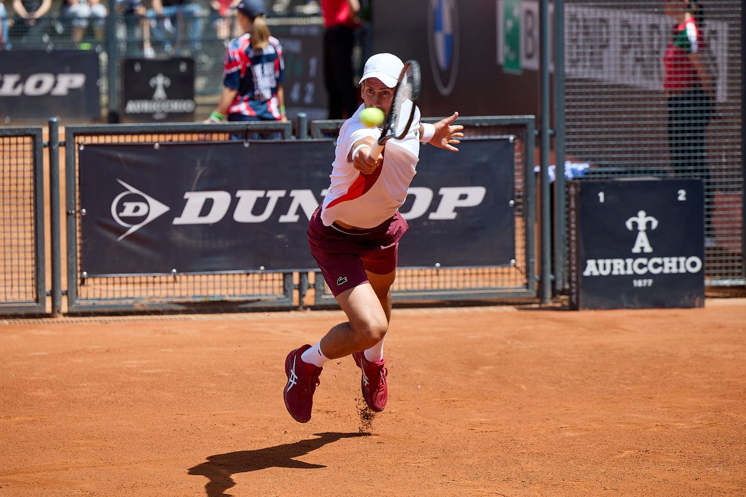 Tennis player jumps to hit overhead shot on clay court during match.