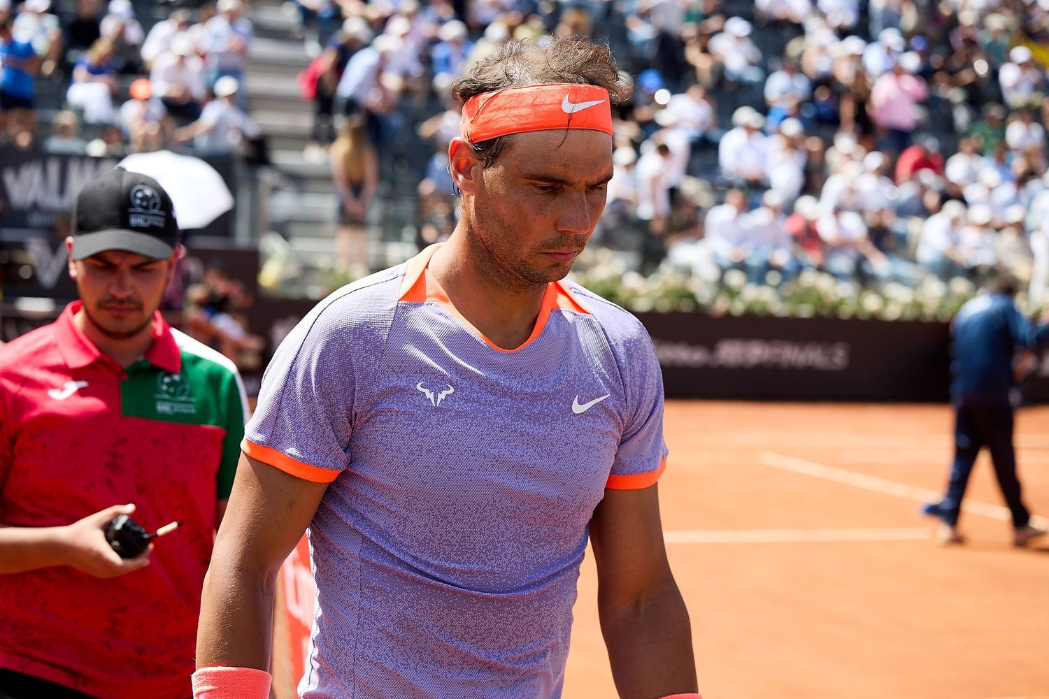 Tennis player in pink and purple outfit wipes sweat during clay court match.