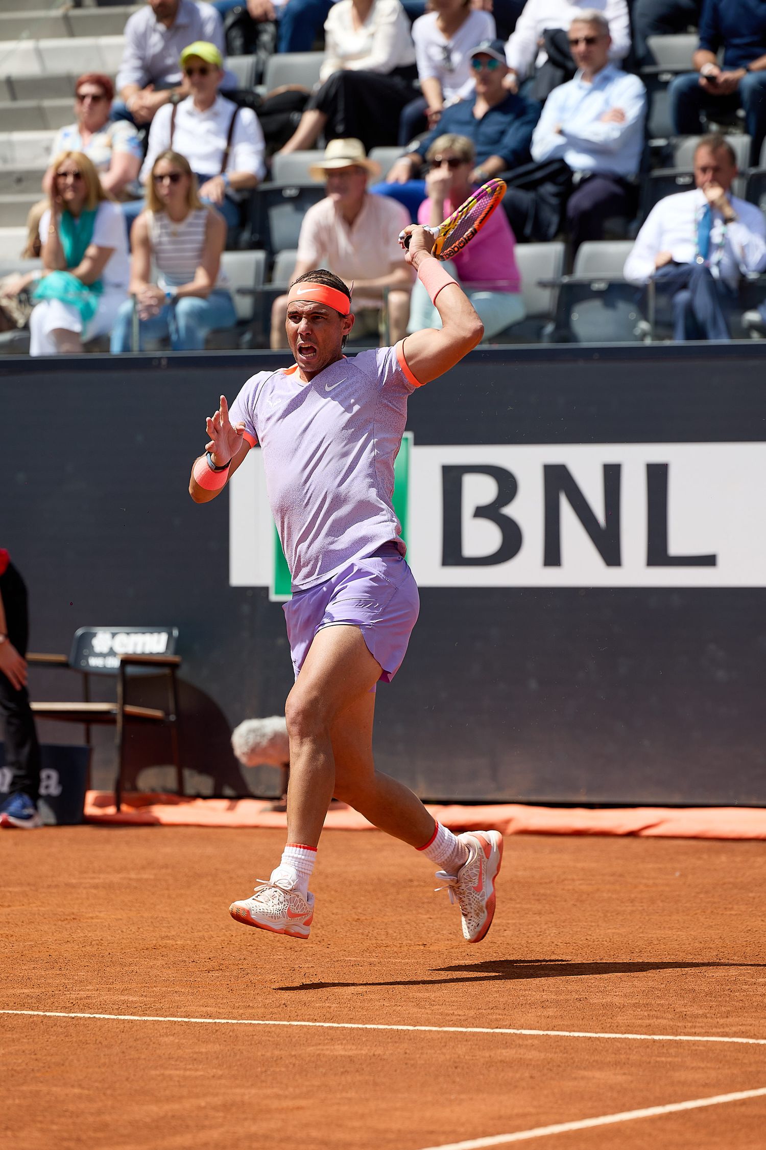 Tennis player in light colored outfit hits powerful serve during clay court match.