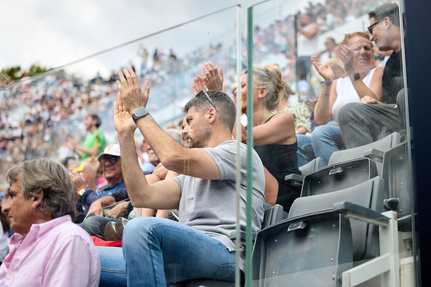 Crowd of spectators cheering and clapping in stadium seating.