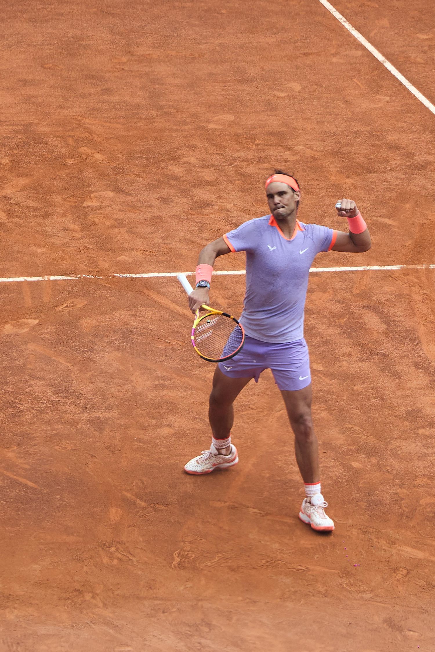 Tennis player in purple outfit following through on forehand shot on clay court.